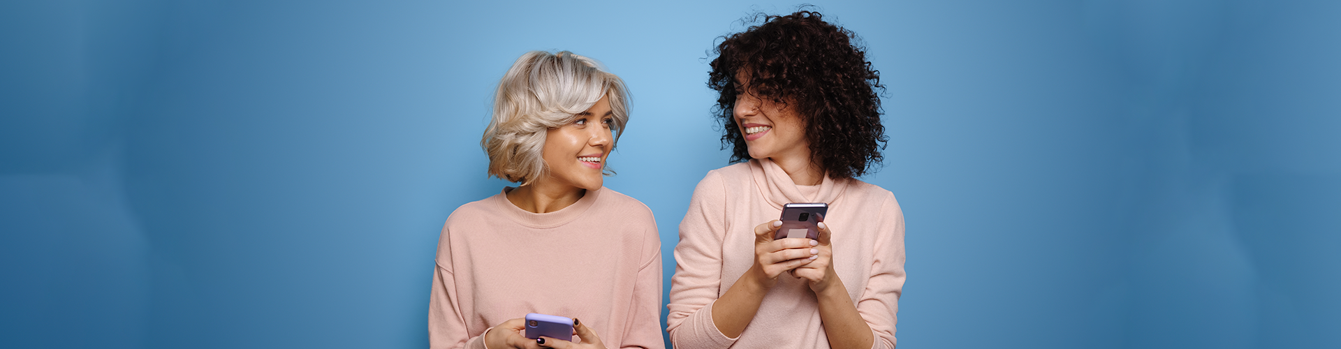 two ladies looking at each other with cell phones in hand